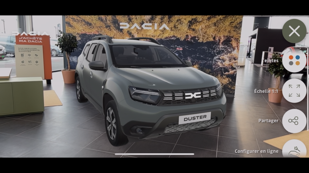 Vue de l'application Dacia AR : un Duster gris en réalité augmentée dans un showroom, avec les commandes Teintes, Échelle 1:1, Partager et Configurer en ligne.