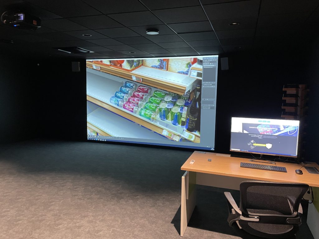 Le mur immersif de l'ESEPAC affiche un linéaire de boissons modélisé en 3D ; un poste de pilotage avec écran est installé sur le côté.